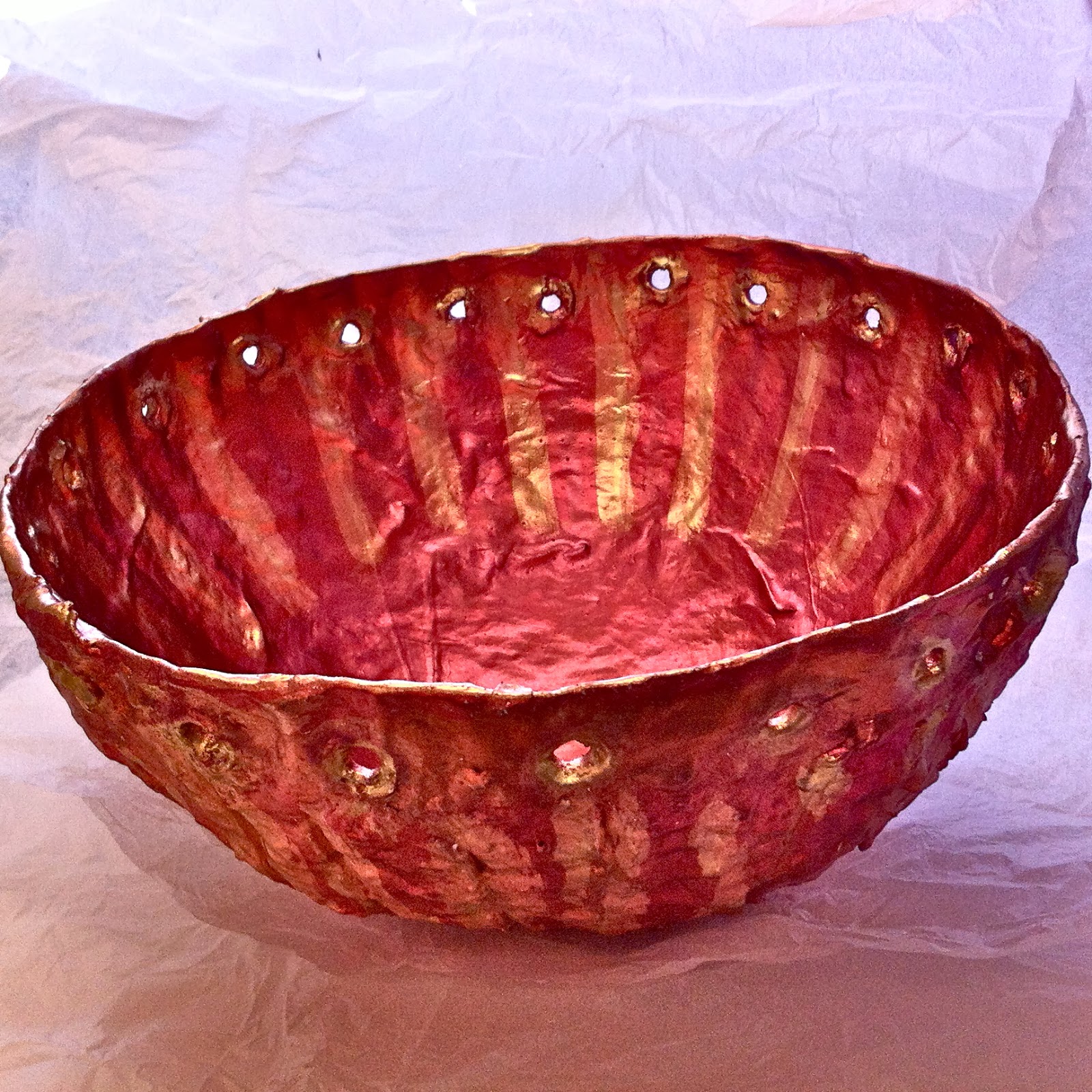 A red paper mache bowl with a creased surface and golden marks