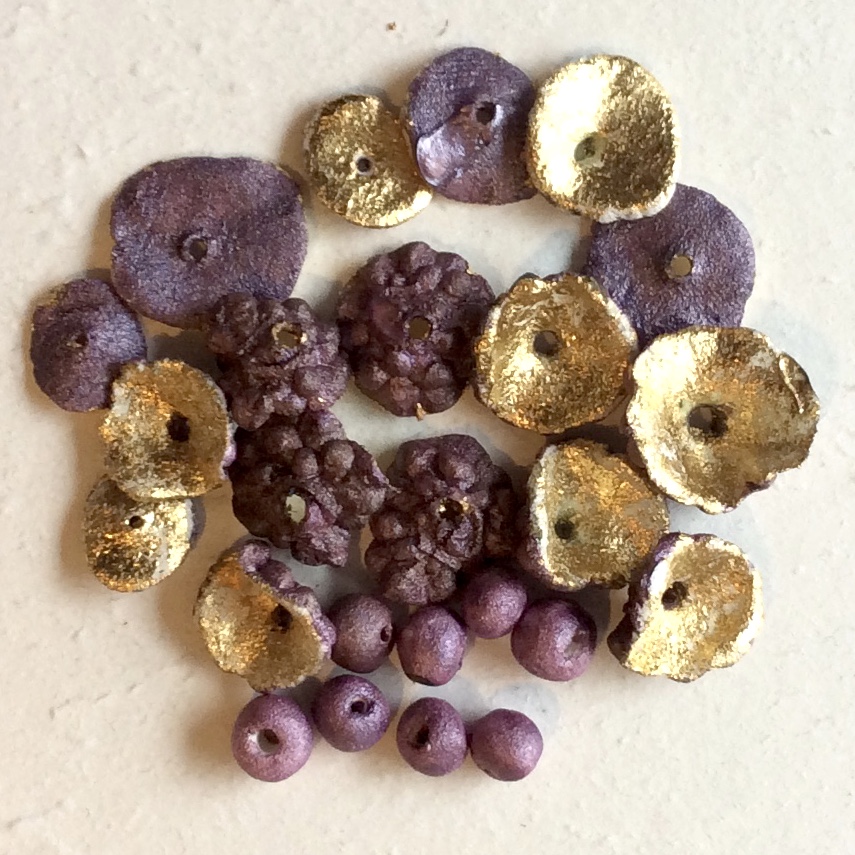 Purple and gold paper mache beads arranged on a pale surface